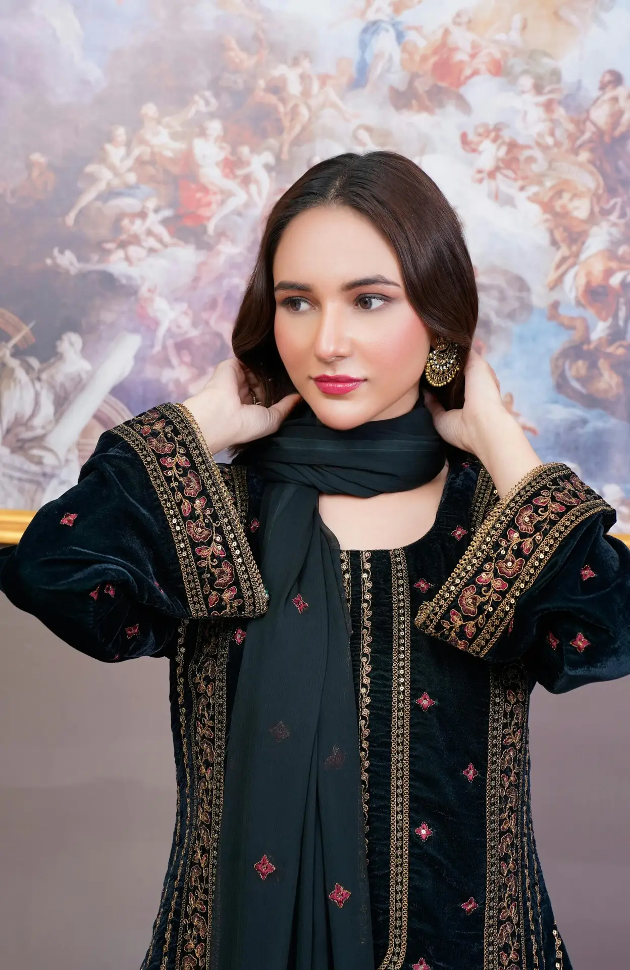 A fashionable young woman in traditional Pakistani attire, elegantly posed indoors.