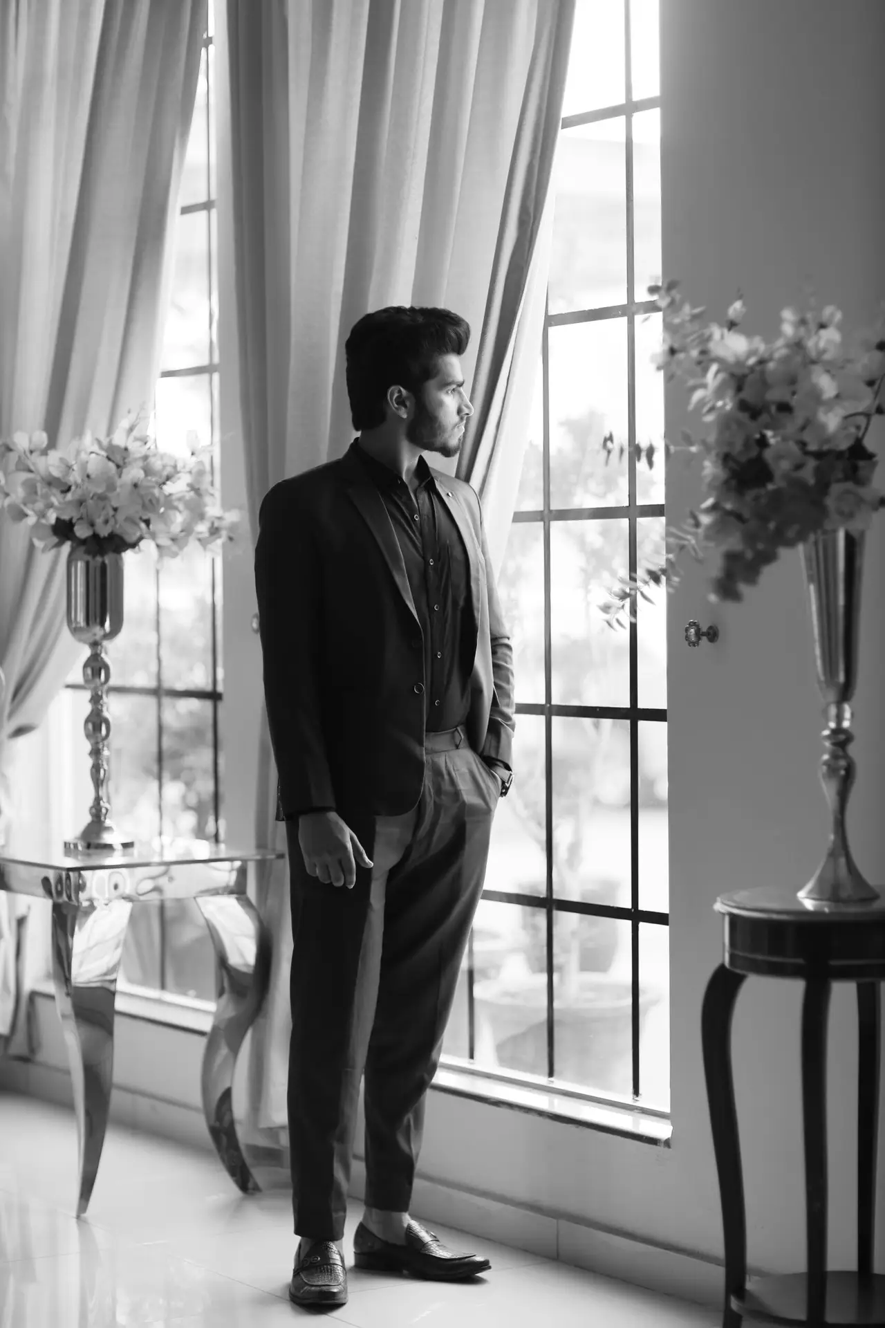 Stylish man in a suit looking out the window in black and white ambiance indoors.
